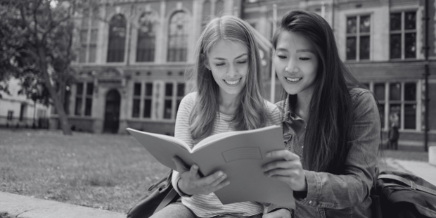 Two women look at a workbook outside at a college campus