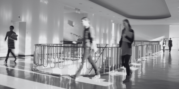 Blurred figures walk in a hallway above a staircase
